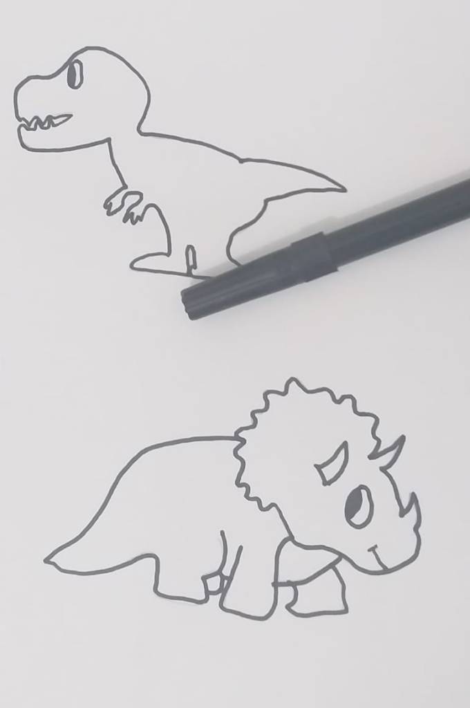 Imagem contendo uma folha de papel com o desenho de dois dinossauros. Por cima, há uma caneta de cor preta.