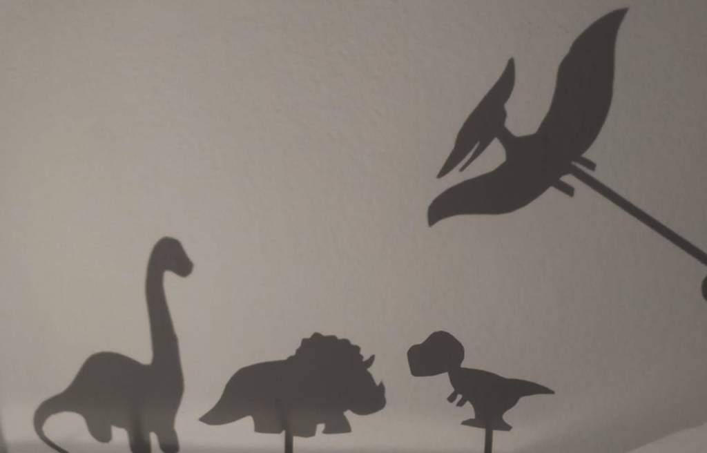 Imagem composta de quatro sombras na parede, cada uma possui o formato de um dinossauro.