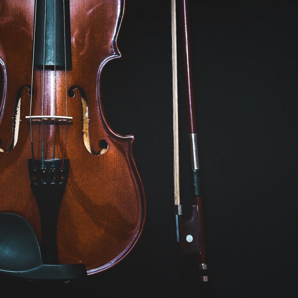 Foto de um violino e um arco de violino, ao seu lado, em um fundo preto.
